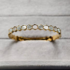 Close-up of gold honeycomb bracelet with embedded crystals on gray fabric background