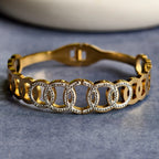 Gold bracelet with interlocking circular links embellished with clear rhinestones on gray surface