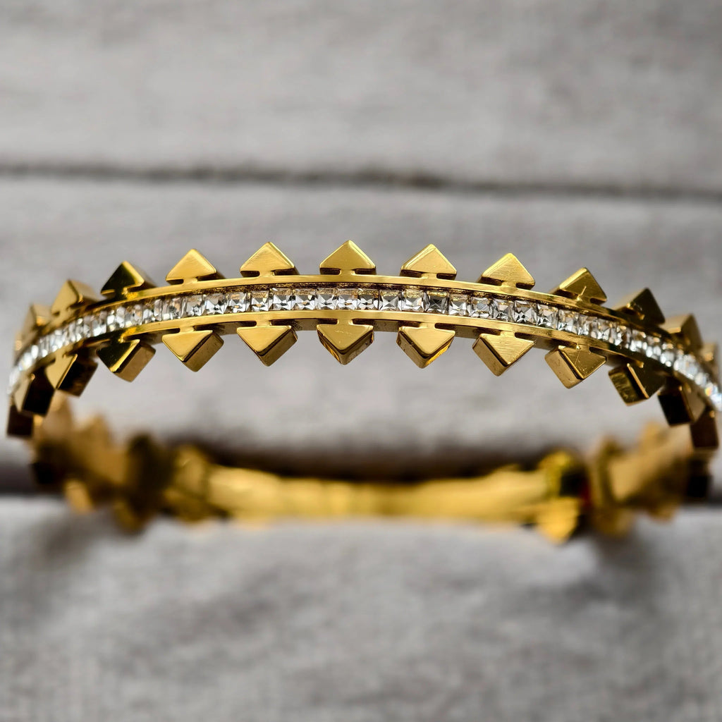 Gold bracelet with pyramid studs and row of clear square gemstones on gray background