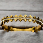 Gold bracelet with pyramid studs and row of clear square gemstones on gray background