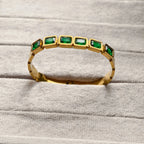 Gold bracelet with rectangular green gemstones on soft gray fabric background