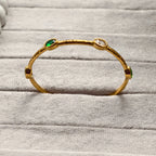 Gold bangle bracelet with green, red, and clear gemstones on gray fabric