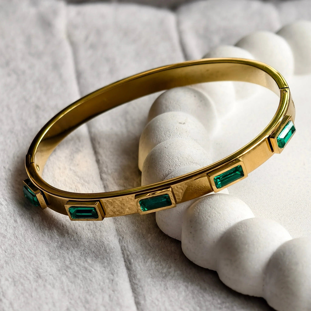 gold bangle bracelet with rectangular green gemstones on white textured surface