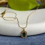 Gold pendant necklace with rectangular green gemstone surrounded by small clear crystals