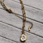 Gold chain necklace with white enamel pendant featuring a floral design on soft gray fabric