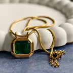 Gold necklace with octagonal green gemstone pendant on blue surface with white textured dish