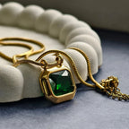 Gold pendant necklace with large green gemstone on white textured display and dark surface