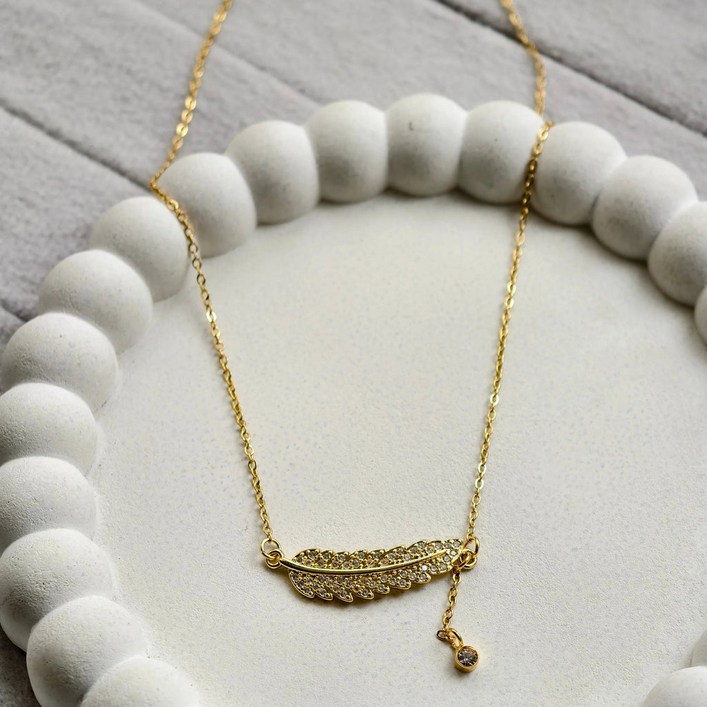 Gold feather necklace with embedded crystals on white textured circular dish
