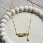 Gold feather necklace with embedded crystals on white textured circular dish