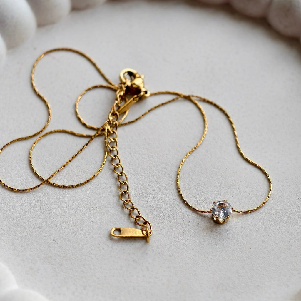 Gold necklace with a clasp on a white ceramic dish