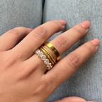 Hand wearing multiple gold rings on a light blue denim background