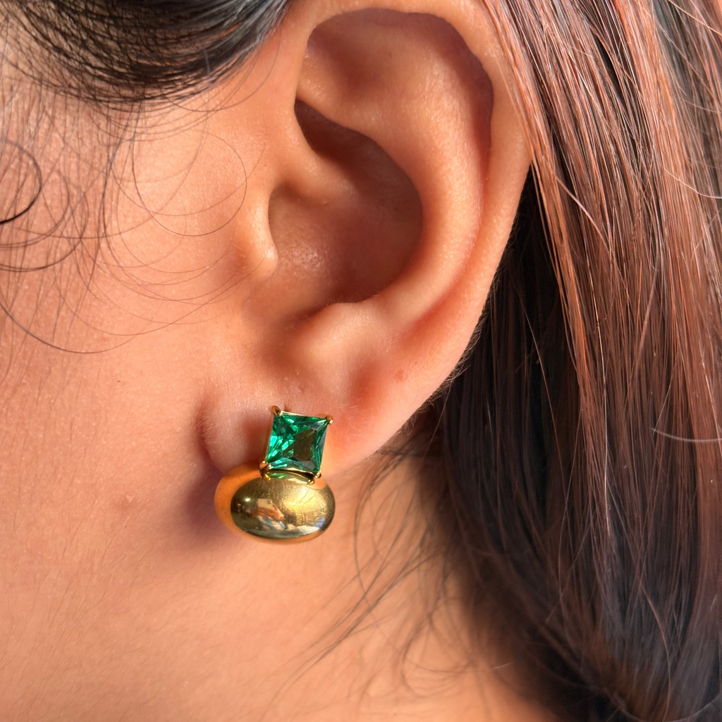 Close-up of an ear wearing a gold earring with a green gemstone.