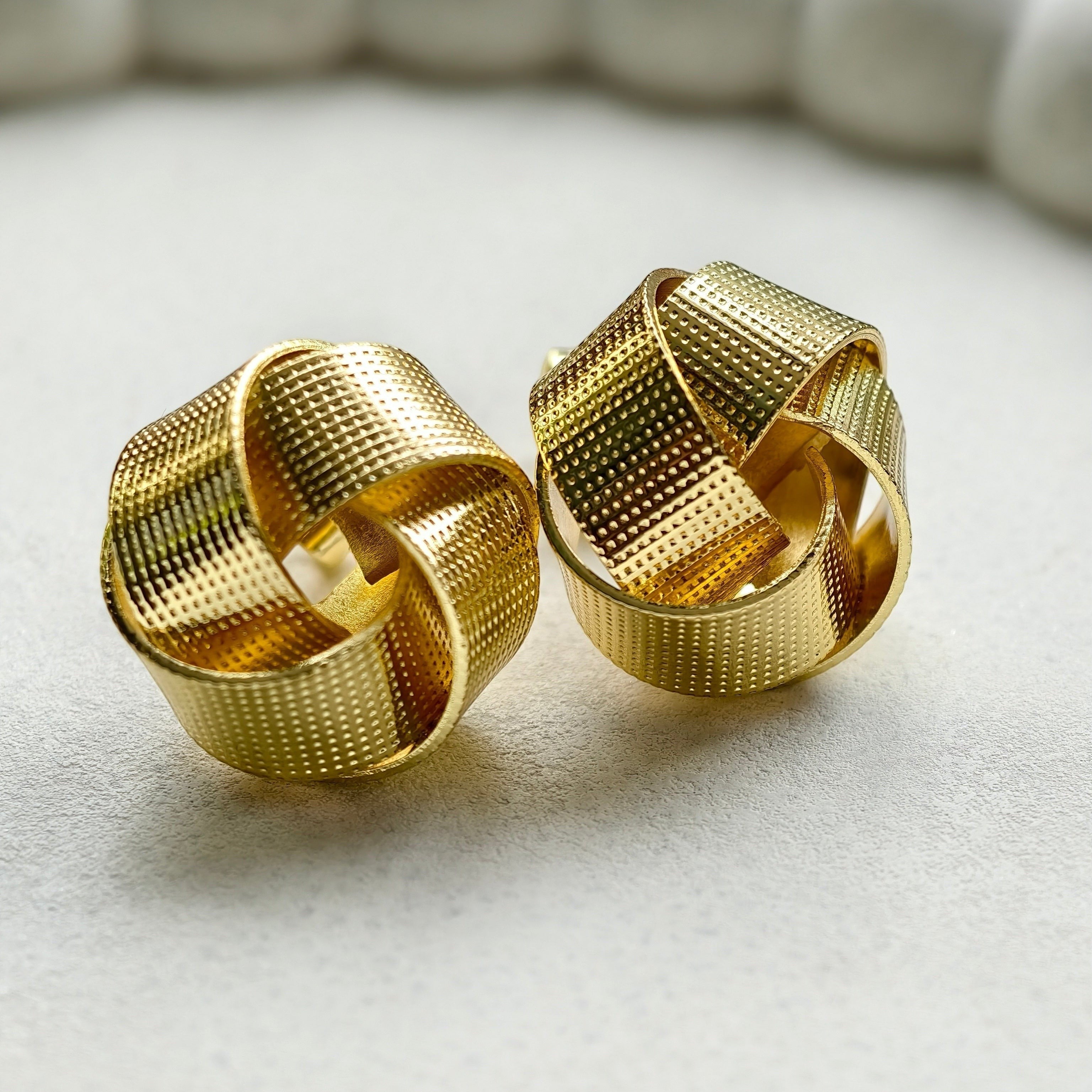 Pretty Shimmering Things Global Nova woven knot stud earrings in 18K gold-plated stainless steel with textured finish.