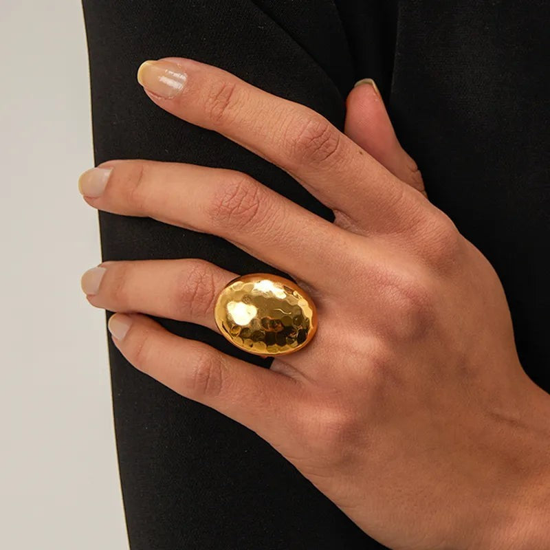 Pretty Shimmering Things Global Zoe hammered gold dome ring on a finger, featuring a large oval textured design.