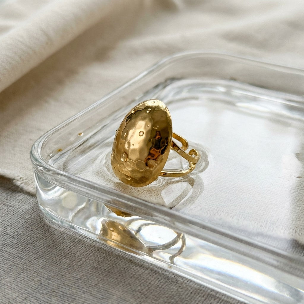 Pretty Shimmering Things Global Zoe hammered gold dome ring with an adjustable open band on a glass tray.