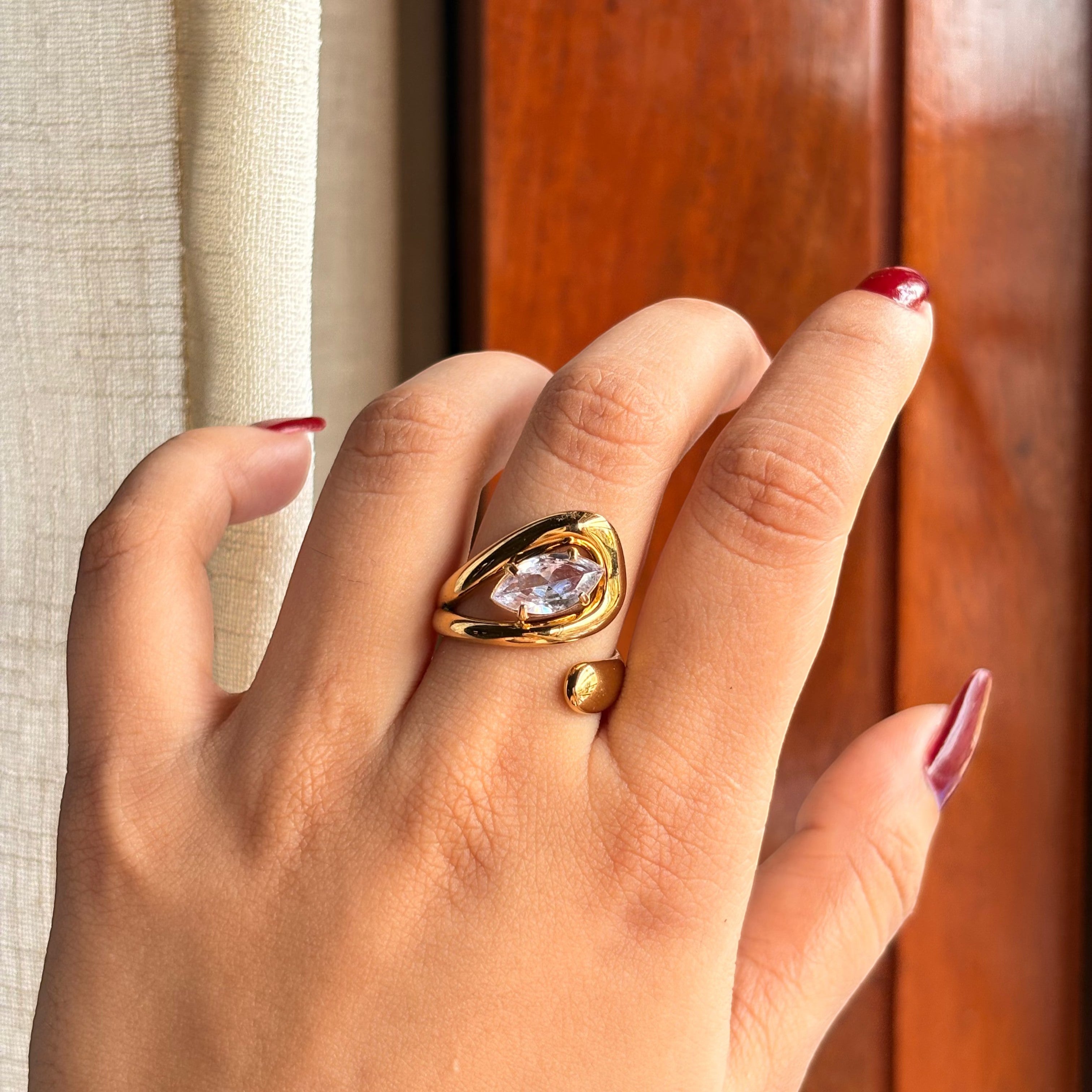 Pretty Shimmering Things Global Zaria sculptural gold open ring with a clear stone on a hand with red nail polish