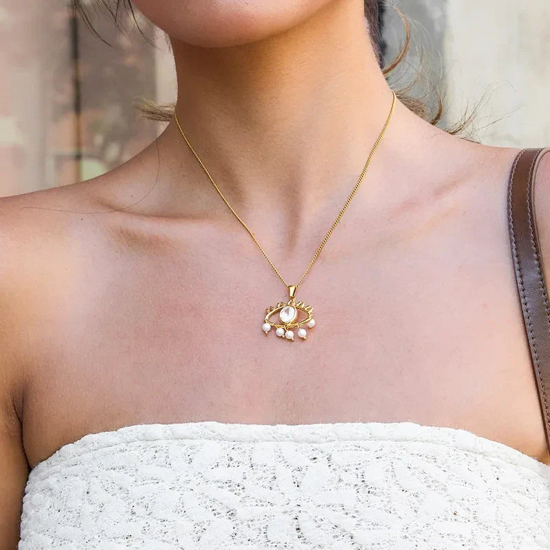 Pretty Shimmering Things gold-tone stainless steel evil eye necklace with central crystal and dangling faux pearls.